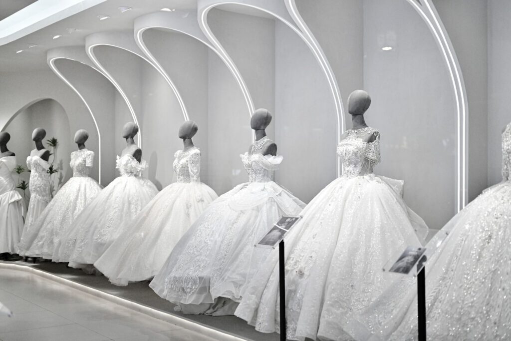 Fila di abiti da sposa ampi e ricamati su manichini, sotto archi illuminati in uno showroom bianco