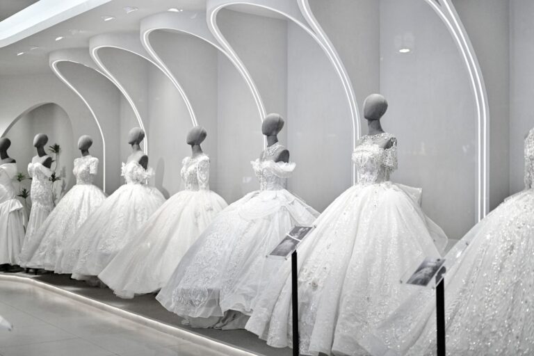 Fila di abiti da sposa ampi e ricamati su manichini, sotto archi illuminati in uno showroom bianco