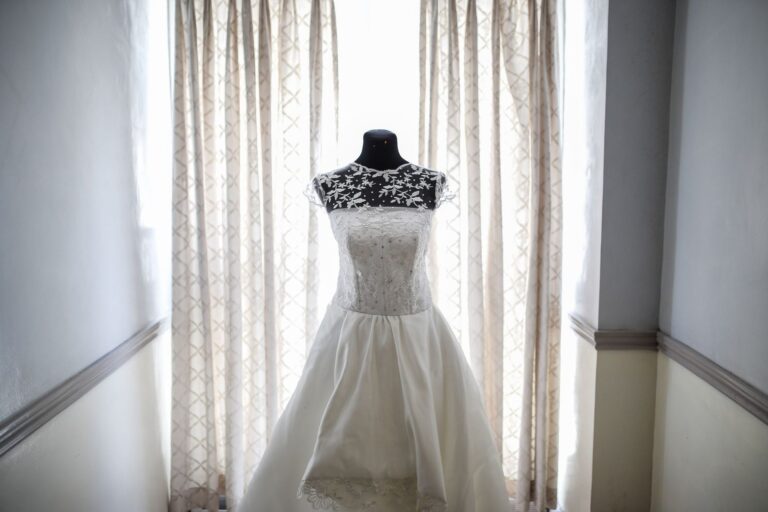 Abito da sposa con corpetto in pizzo ricamato su manichino, davanti a una finestra luminosa